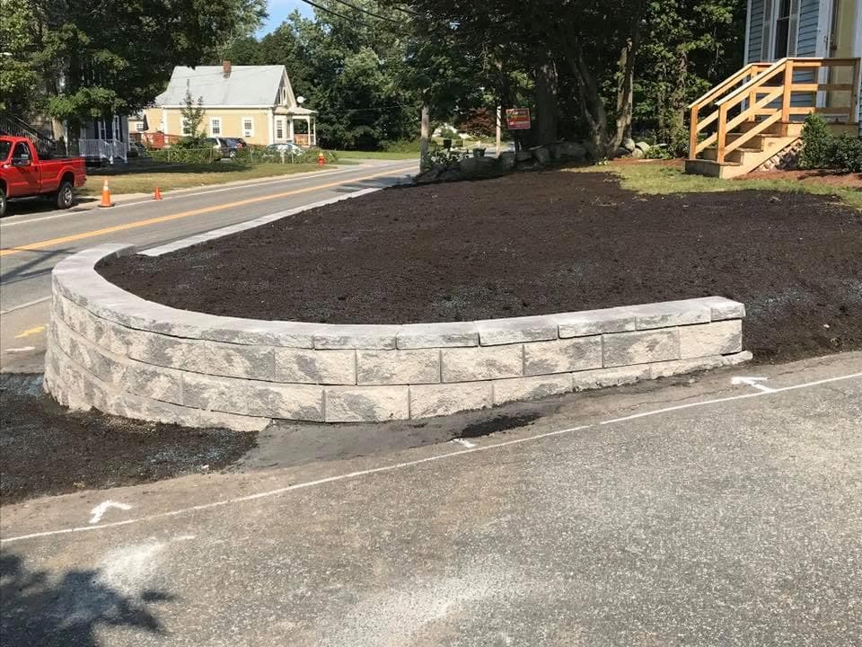 Curved block retaining wall holding fresh loam along a roadside.