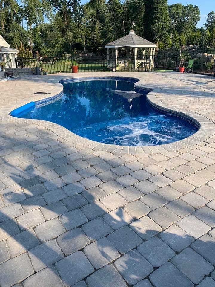 Freeform swimming pool ringed by a full paver patio surround.