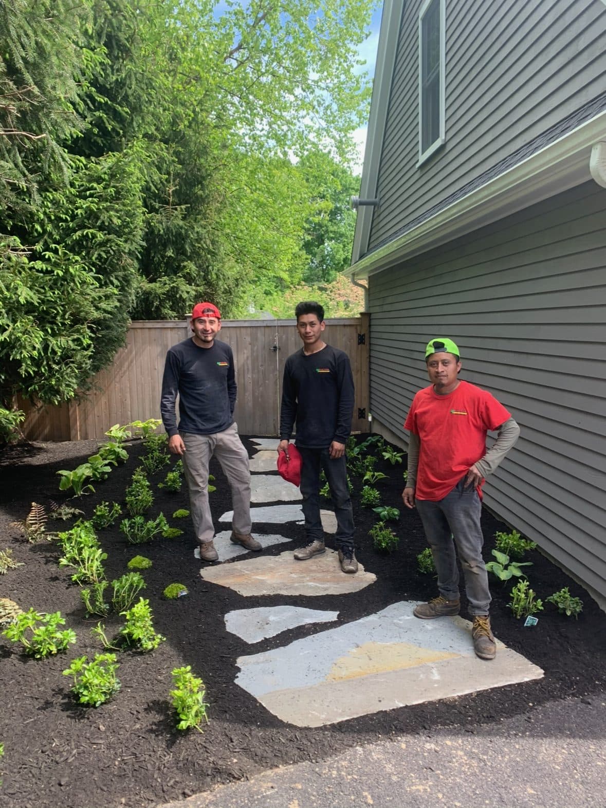 Three of the Keith White Landscaping crew on a finished flagstone path they have just laid, with new plantings either side.