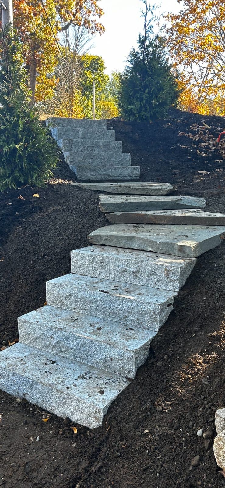 Granite steps and flagstone treads on a graded slope with autumn foliage behind.