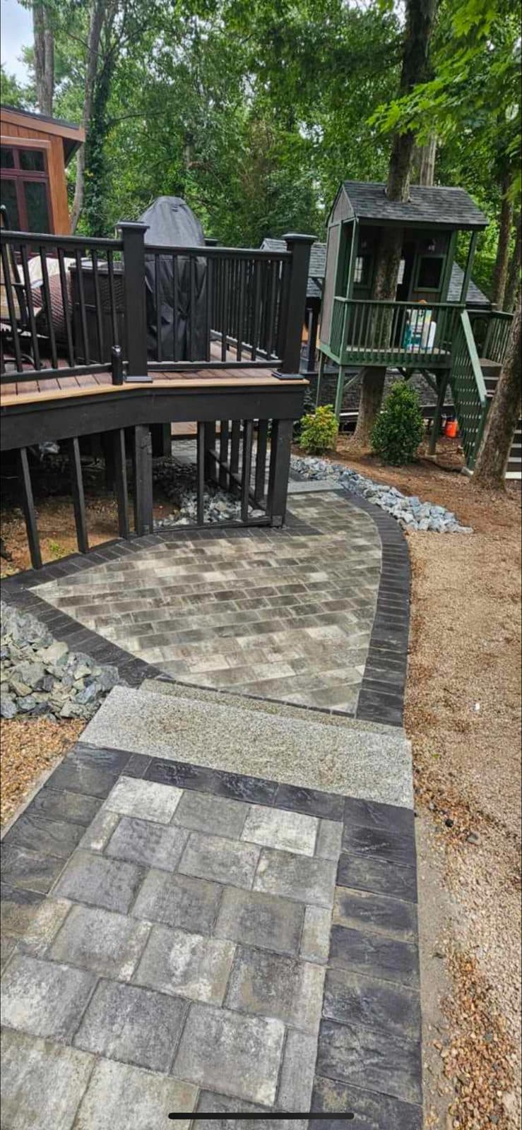 Paver walkway and patio set below a raised deck, with a drainage stone bed running along the edge.