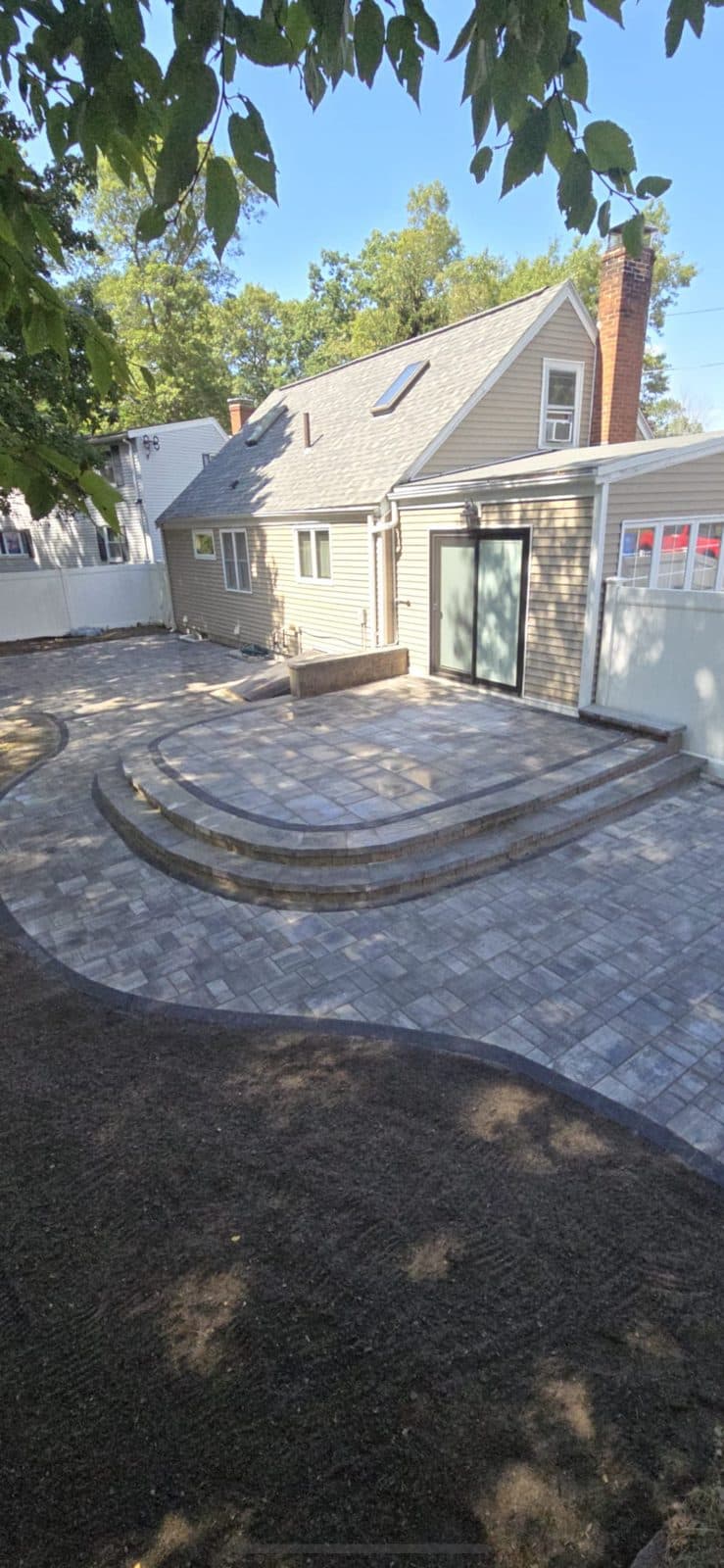 Paver patio with curved stepped seating area behind a house, bordered by fresh mulch beds.