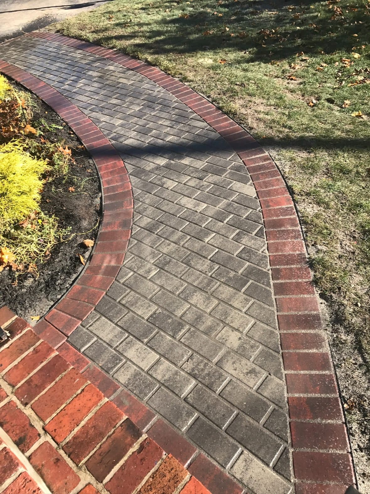 Curved walkway in grey herringbone pavers with a red brick soldier border, meeting a red brick landing.